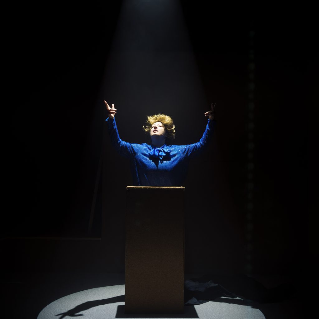 Character dressed as Margaret Thatcher on stage under a spotlight