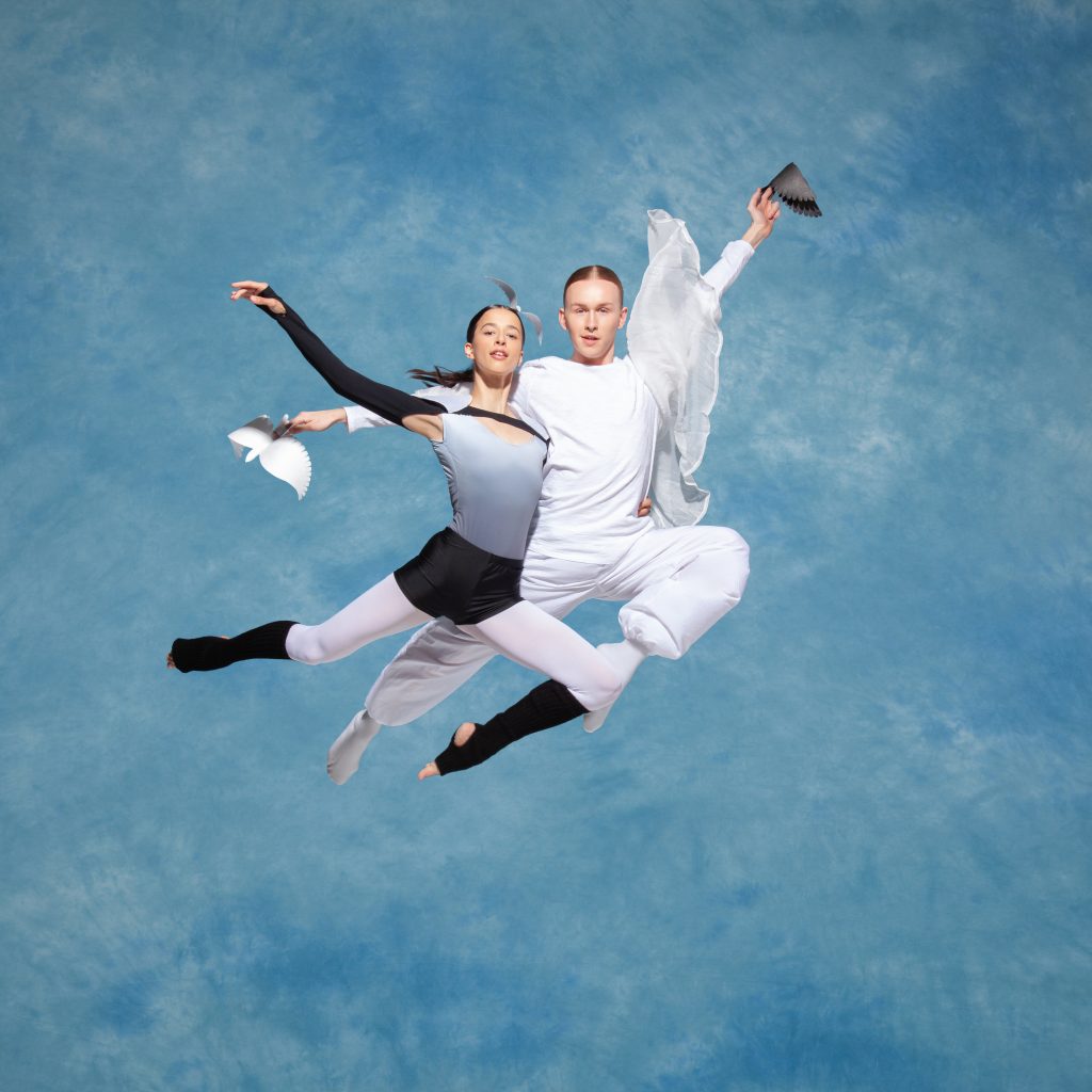 Two dancers posing mid air against a blue sky-like background